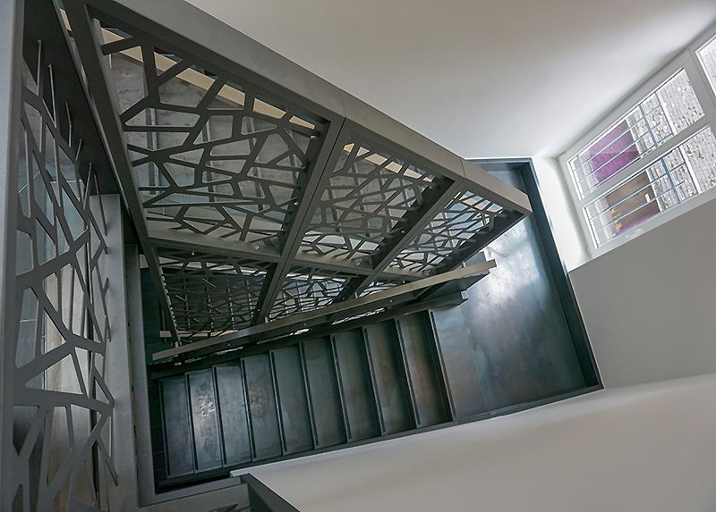 gegenläufige gerade Treppe aus Schwarzstahl (Blaustahl) bestehend aus Treppenwangen und Stahlstufen mit Sicherheitsantrittskante, durchgehendem Treppengeländer im Treppenauge.