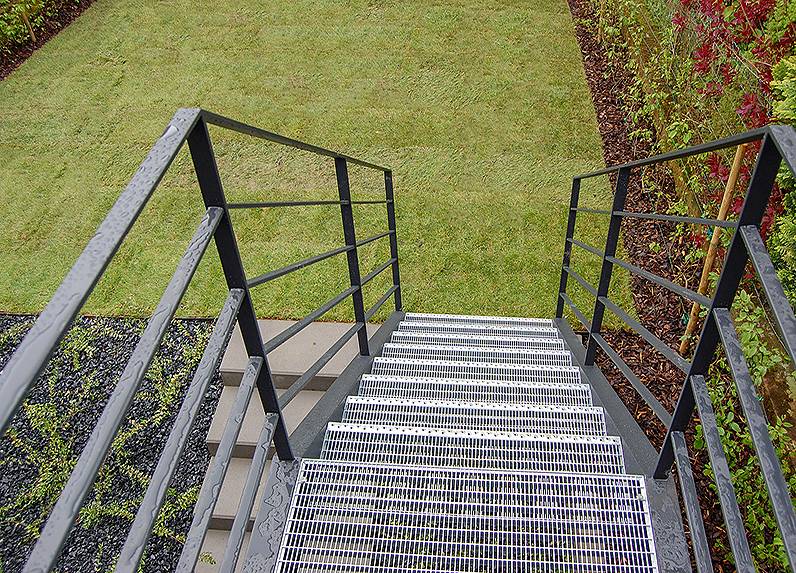 Außentreppe Garten, gestaltet aus U-Stahl lackiert, mit Gitterrsotstufen und einem modernen Geländer aus Flachstahl, Oberfläche in anthrazit pulverbeschichtet.
